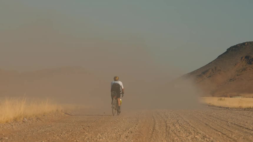 View of a cyclist cycling on a dusty dirt road in a natural environment