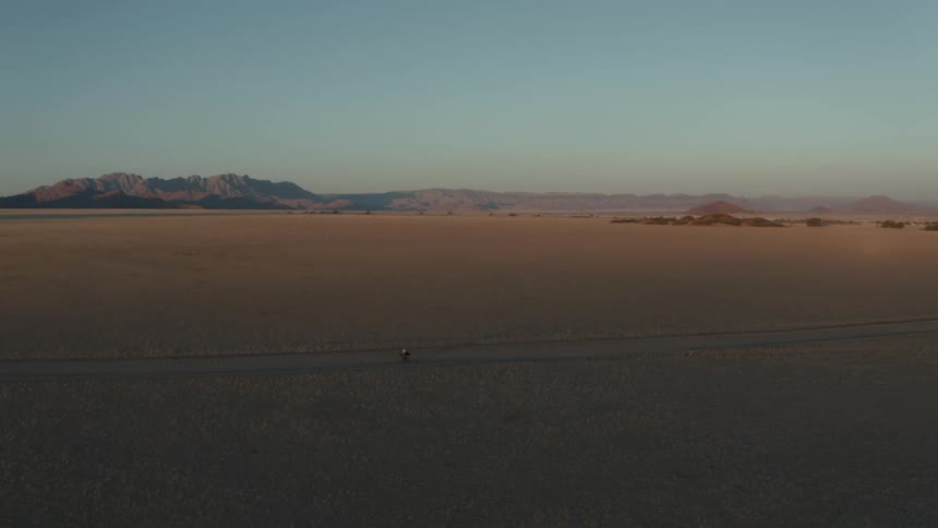 Aerial landscape of a person cycling on a simple street with desert vegetation around them on a blue sky morning