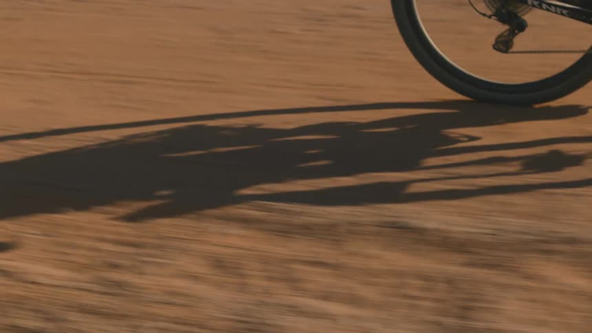 Closeup of the rear wheel of a bicycle with a person pedaling on a dirt floor during the day