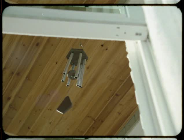 A wind chime outside a window blows around with the wind