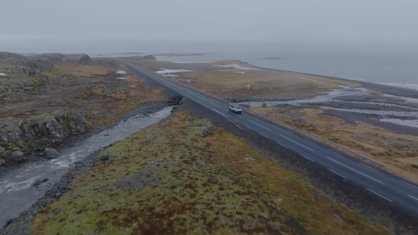 A car driving on an asphalt road that passes over a river and connects to the sea