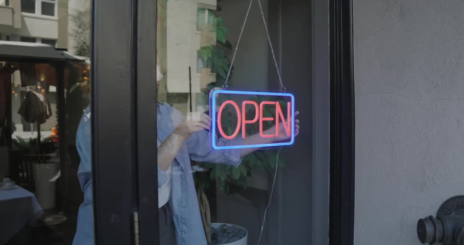 A person is fixing a neon sign that says open on the glass door
