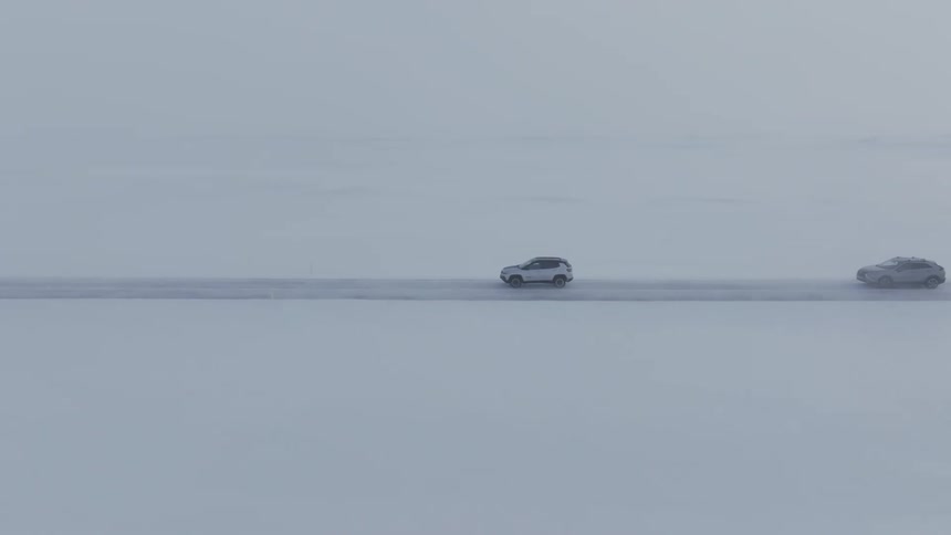 Some cars driving on an asphalt road and all around is white covered with snow
