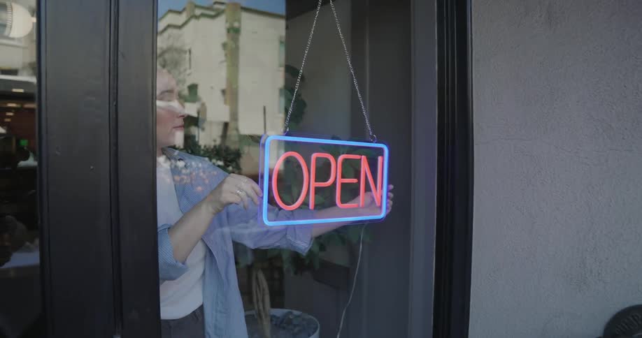 A woman straightens an open sign on the door of a business