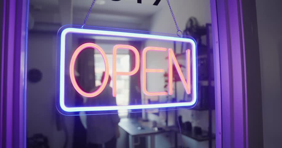 A woman turns on a neon open sign