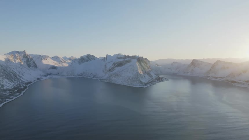 The mountains by the water are covered with snow