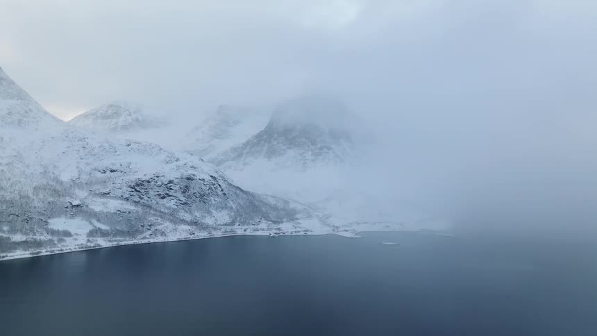 Aerial panorama of a peninsula with mountains on the horizon covered in snow on a foggy day