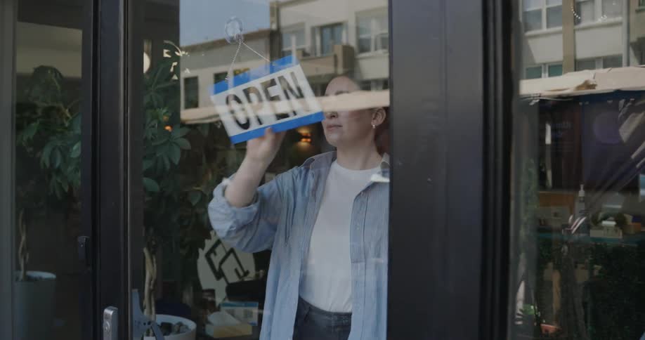 A woman flips a sign from closed to open on a business door