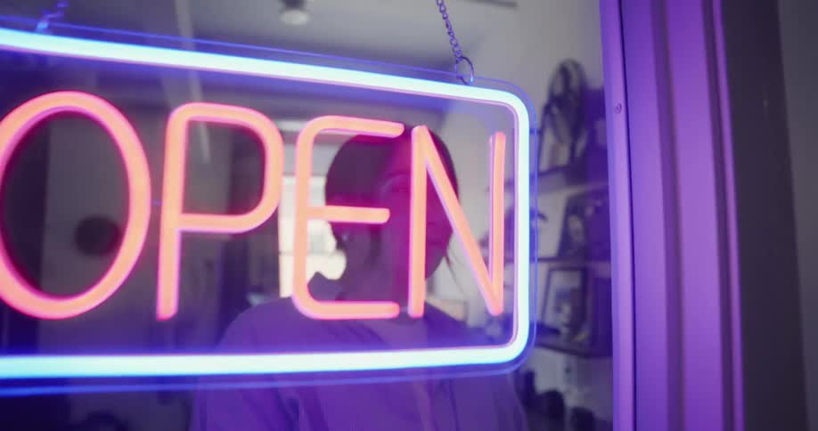 A woman turns on an open sign at a business