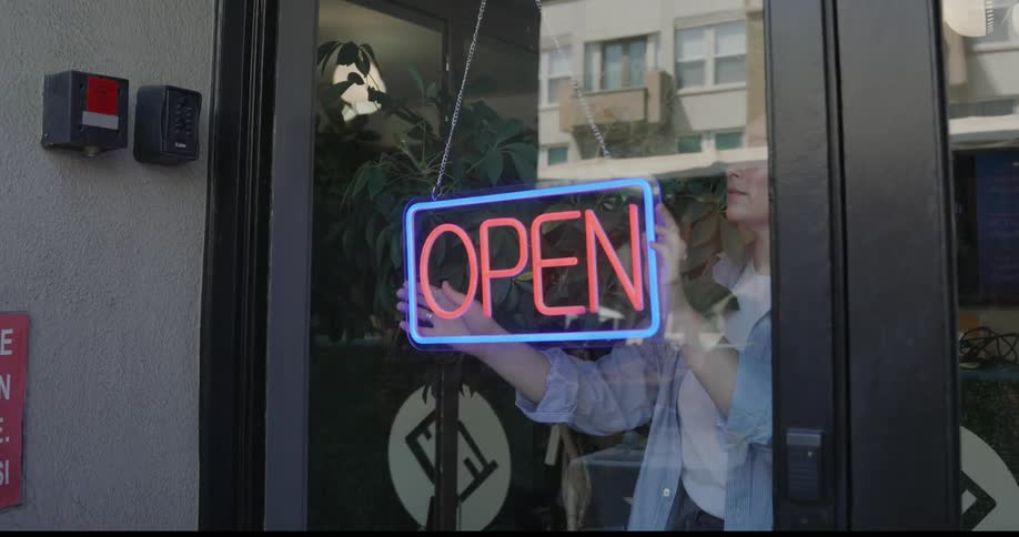 Woman adjusting the open sign on the glass door of an establishment