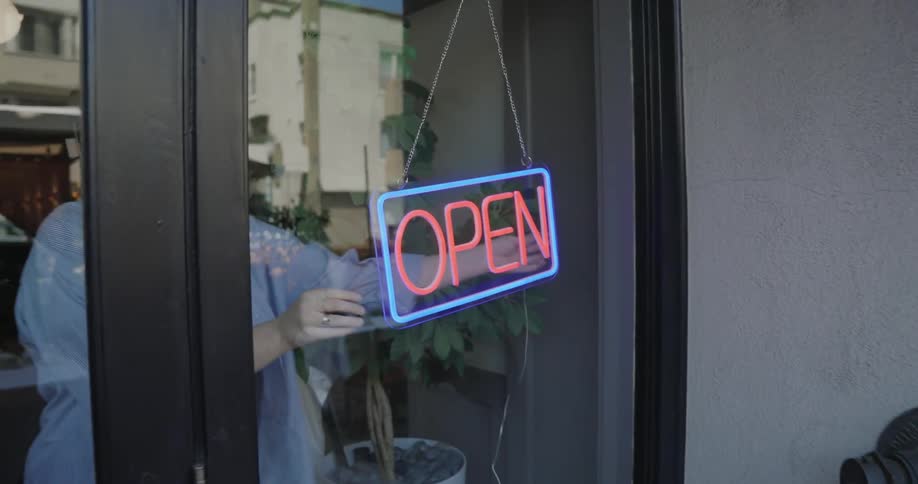 A turning on a neon sign reading open on a glass window