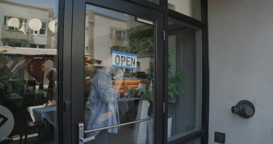 A woman turns a sign that says closed to open on a glass window