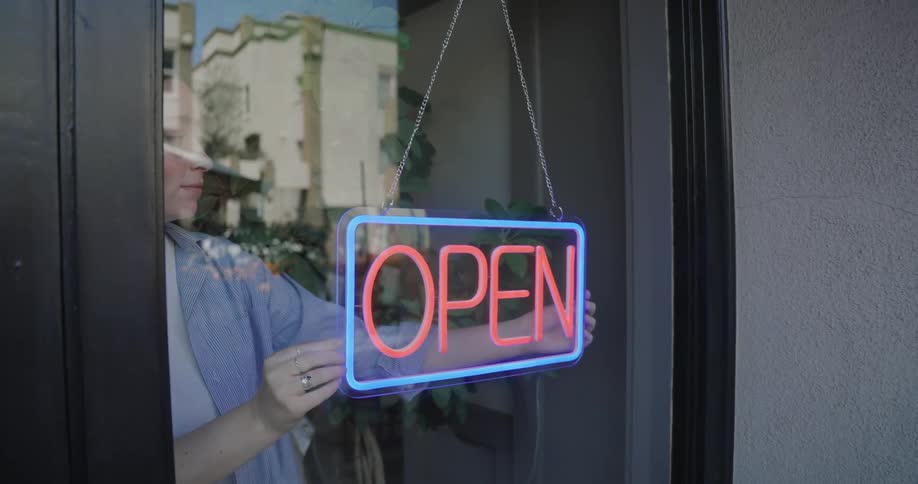 A woman straightens and turns on the open sign in a restaurant