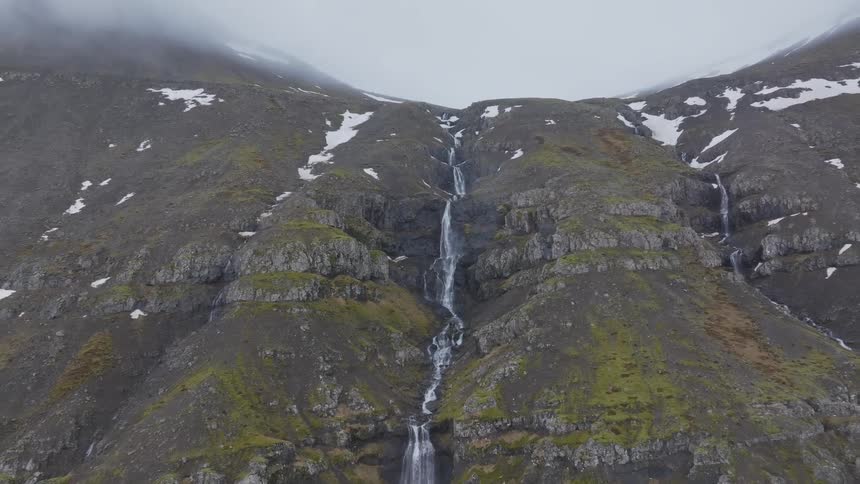 Aerial panorama of a mountain with waterfalls and snow on a cloudy day
