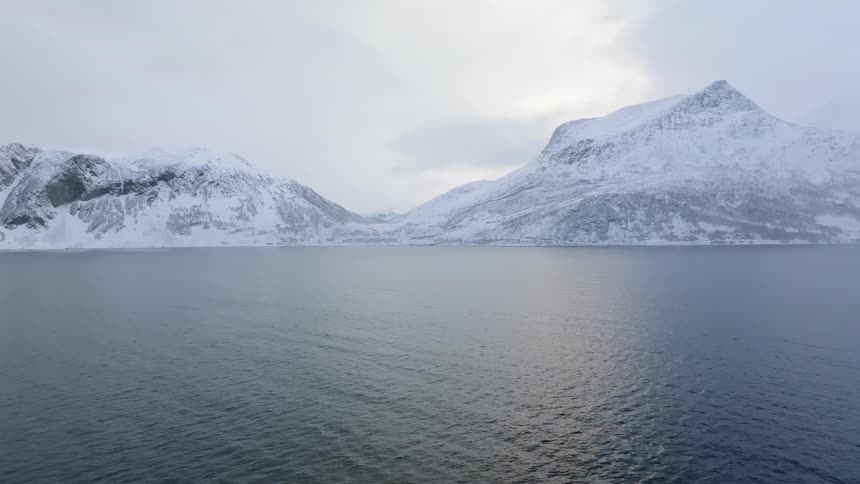 A snowcovered mountain region in front of the ocean that is reflecting light from the sky