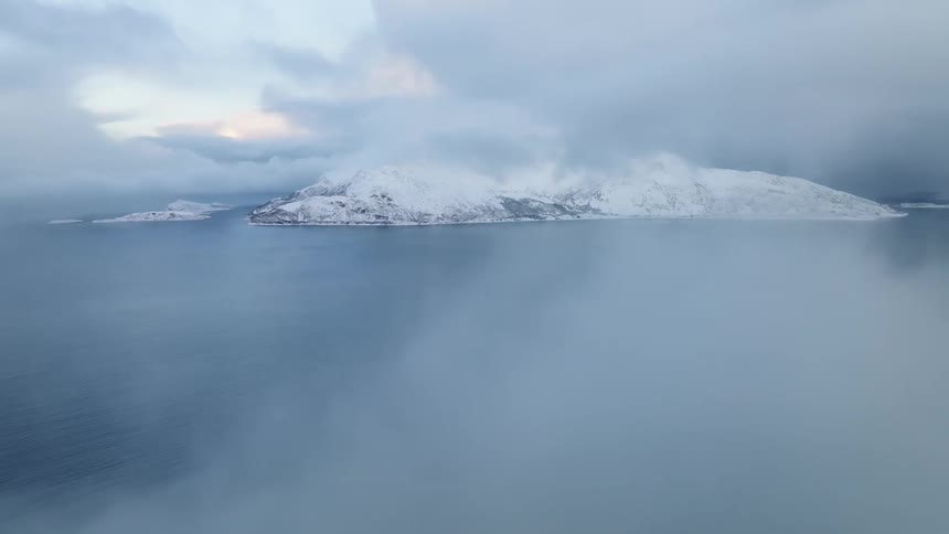 Aerial landscape of a peninsula with snowcapped mountains and a vast blue sea on a foggy day