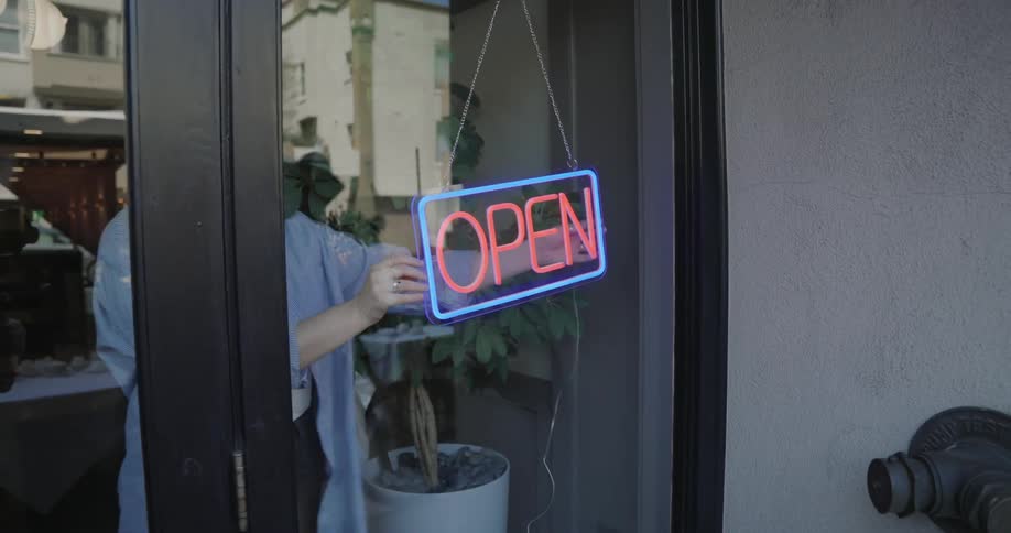 A woman straightens out an open sign on a business door