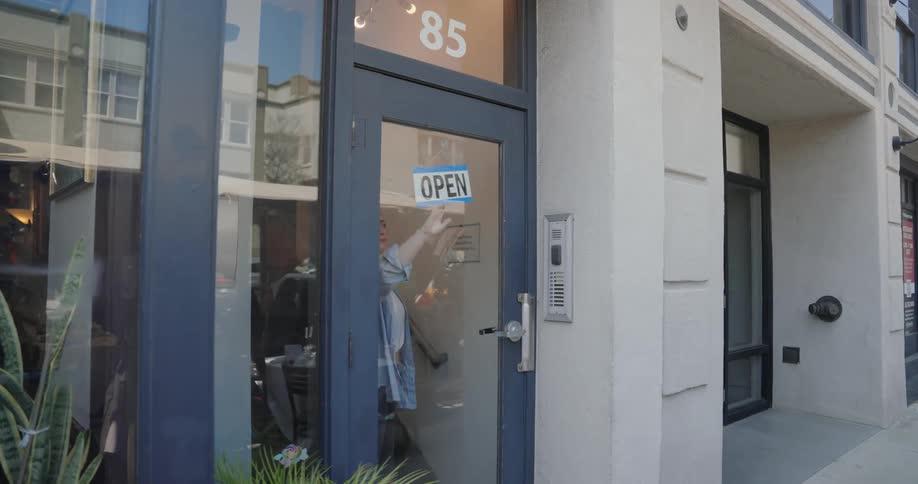 A woman turns a sign in a door to open