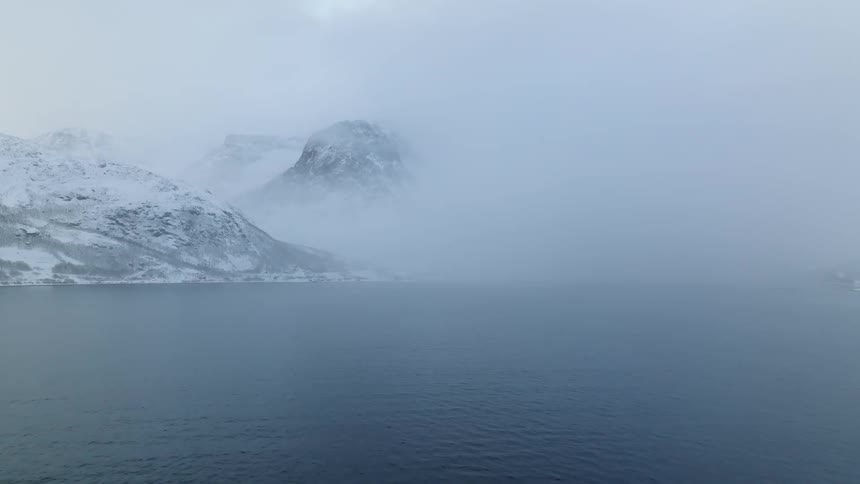 Blue sea landscape with snowcovered mountains on a foggy day