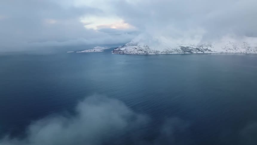 Aerial landscape of a peninsula with blue sea and mountain ranges on the horizon covered by snow on a cloudy day