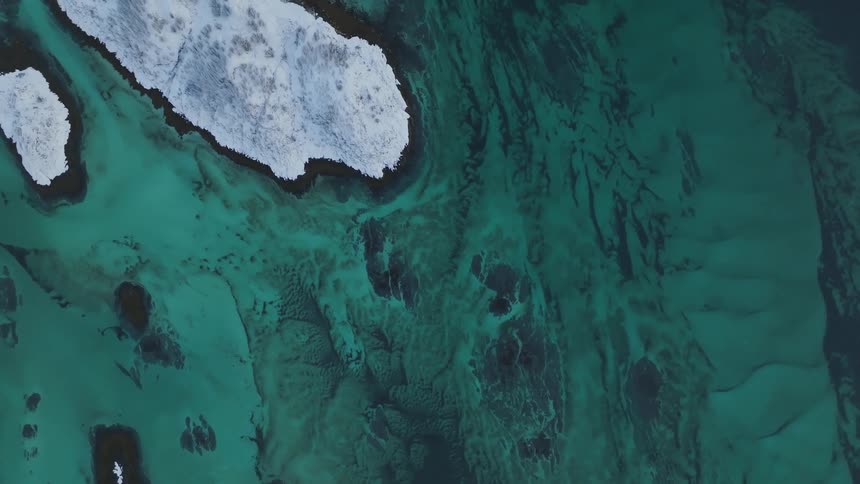 Aerial panorama of a greenish sea with snowy mountains on a peninsula