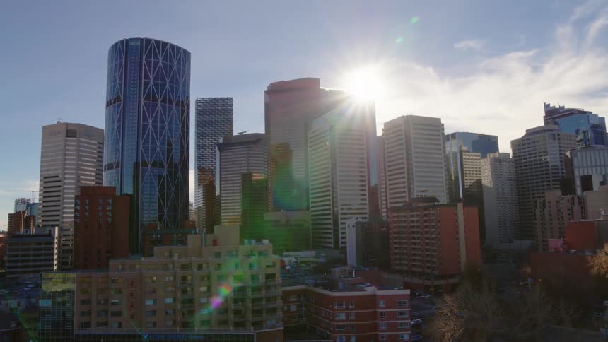 The sun shines out from behind a city center with tall commercial buildings