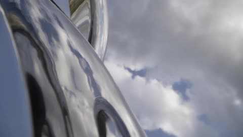 The sky and clouds are reflected on a metallic structure