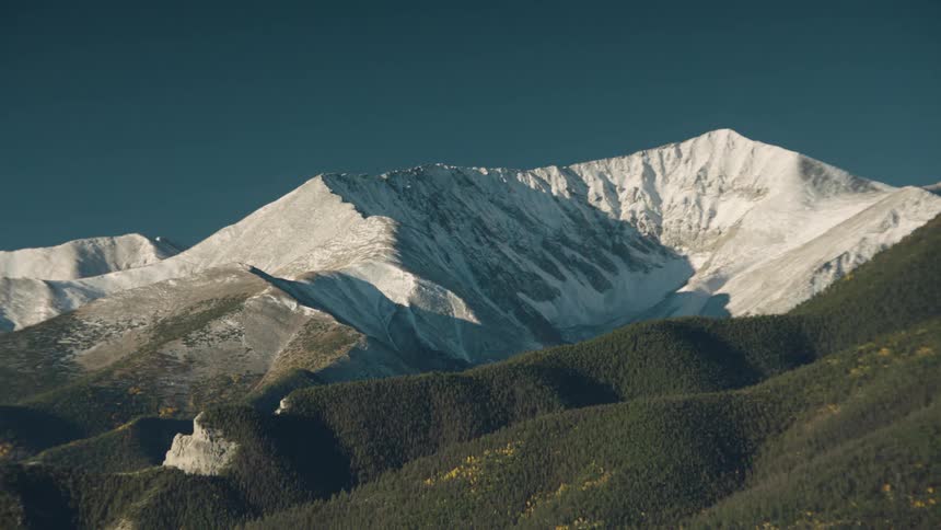 An airplane flying in front of a snowcapped mountain peak under a blue sky with clouds