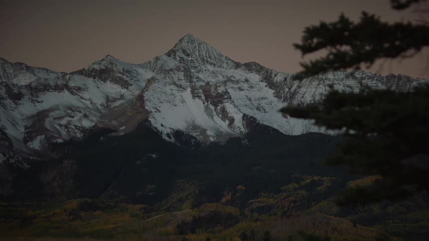 Conifer forest covers lower mountain slopes bordering deciduous trees under a red tinted sky
