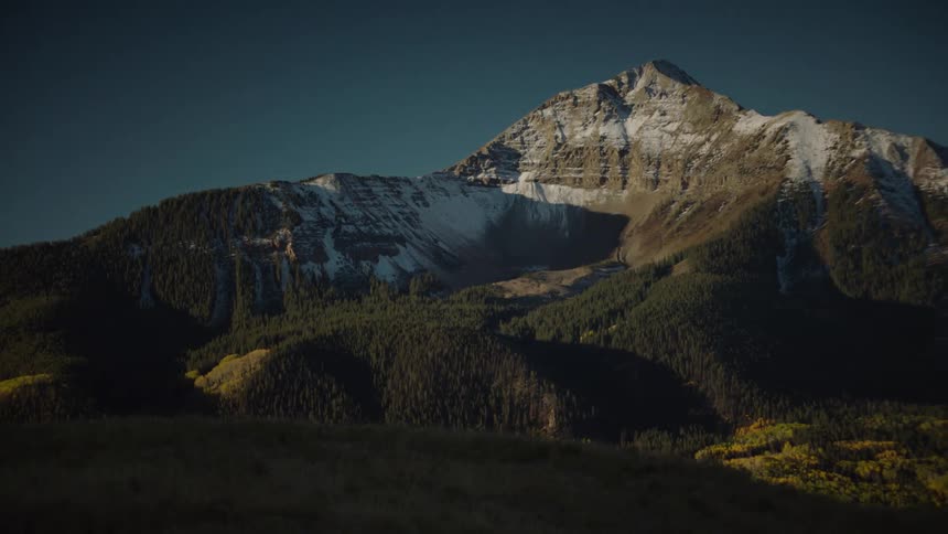 A mountain with a snowcovered peak stands against a clear sky