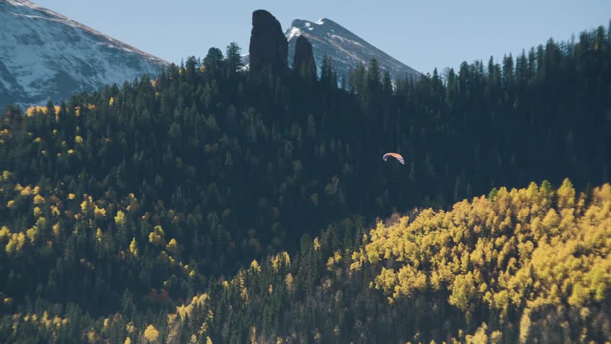 Aerial landscape of mountains with conifers and a person parachuting