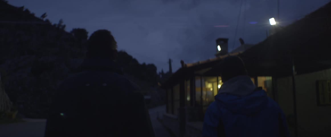 Two people exit a car and walk towards a building at night