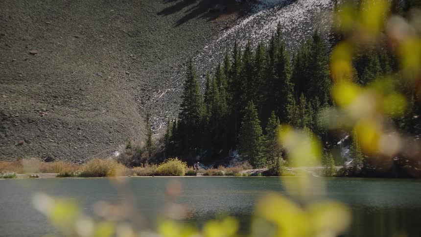 People walking near a lake surrounded by trees on a mountainside