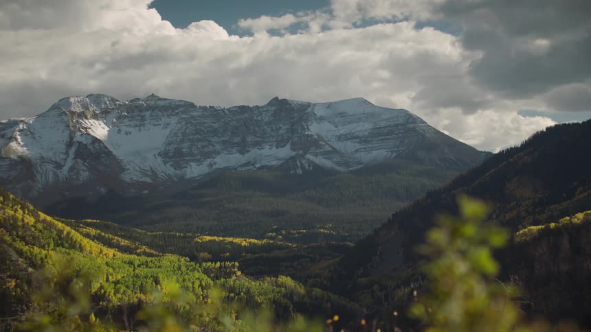 Puffy white clouds over snowcapped mountains and a forested valley