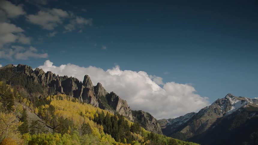 A mountain range of high rocks and lags behind a large white cloud in a blue sky