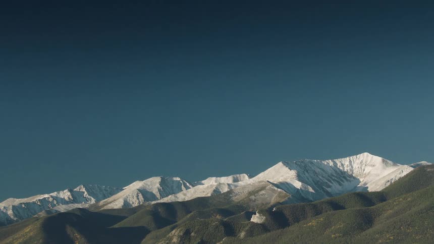 Snow covered mountains border green mountains on a clear day