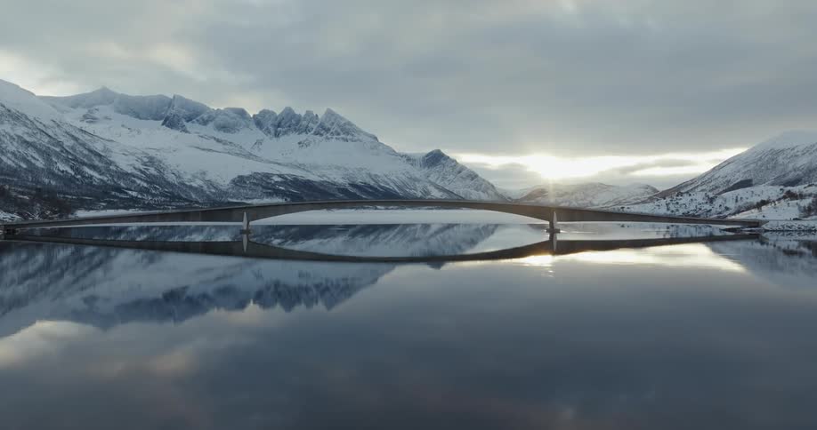 Aerial view of a bridge over a frozen lake nested in the mountains at morning