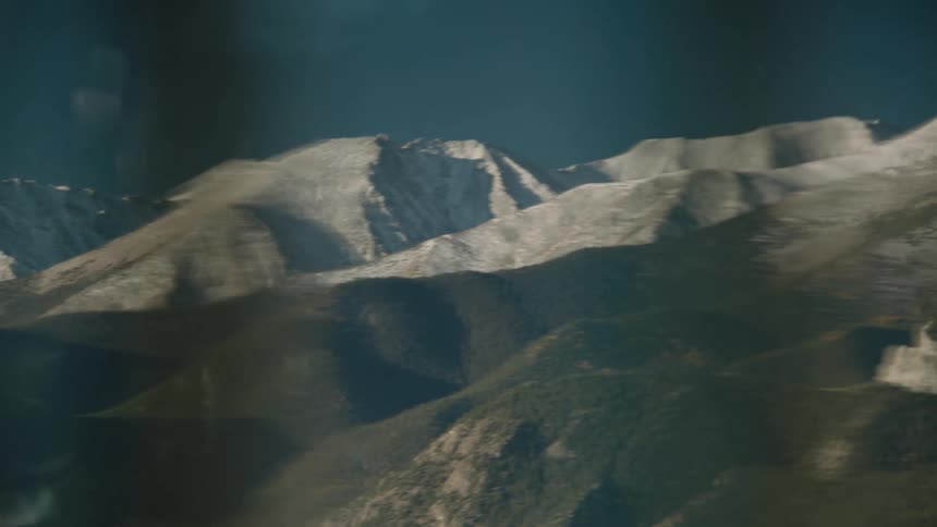 A panoramic view of a mountain range with peaks partially covered in snow seen from a window