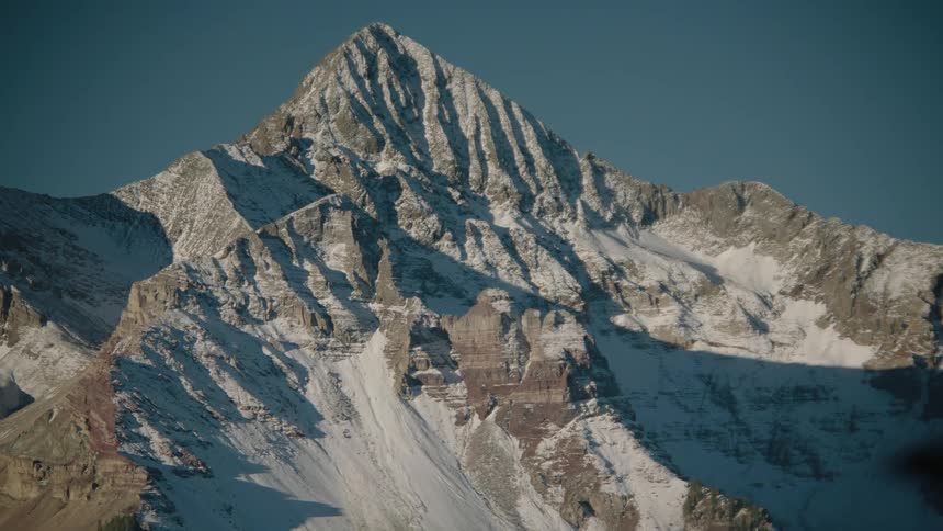 Rocky mountain with cliff and snow against a cloudless blue sky
