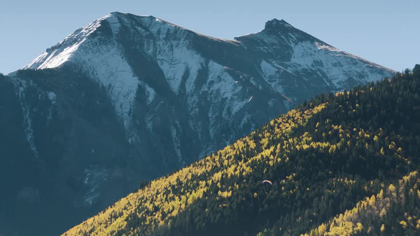 A parachute glides over a forest near mountains