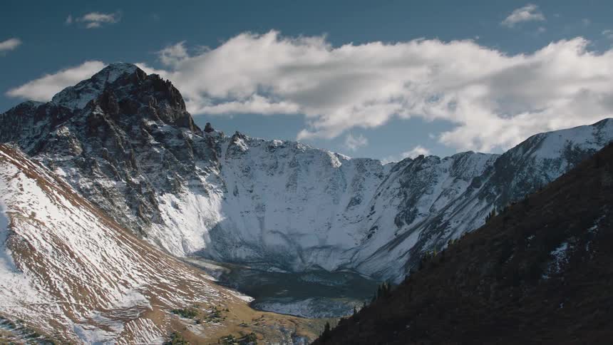Snow covers steep mountain slopes enclosing lake on a cloudy day