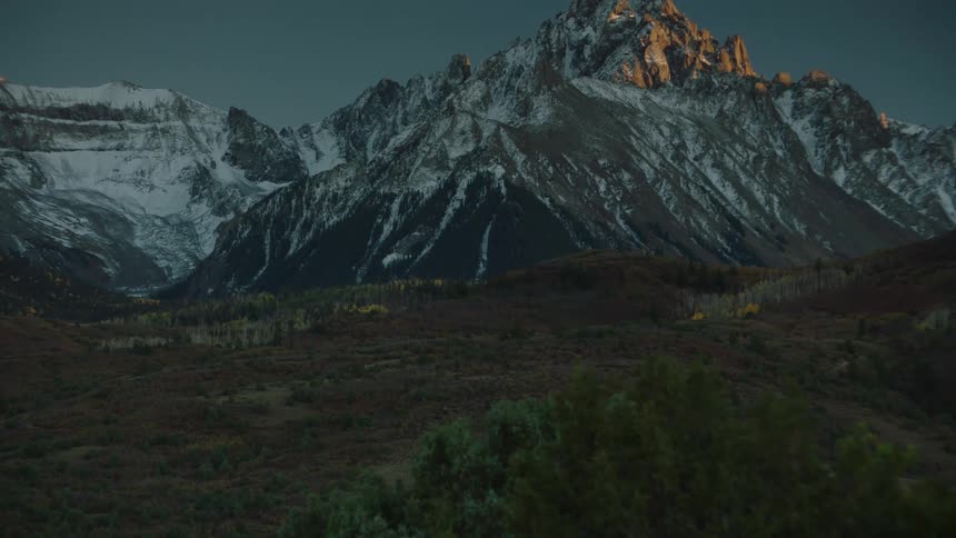 Animals graze in the shadow of a large mountain range