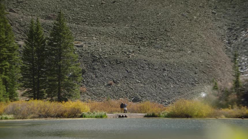 People stand on shore at the base of mountain slope