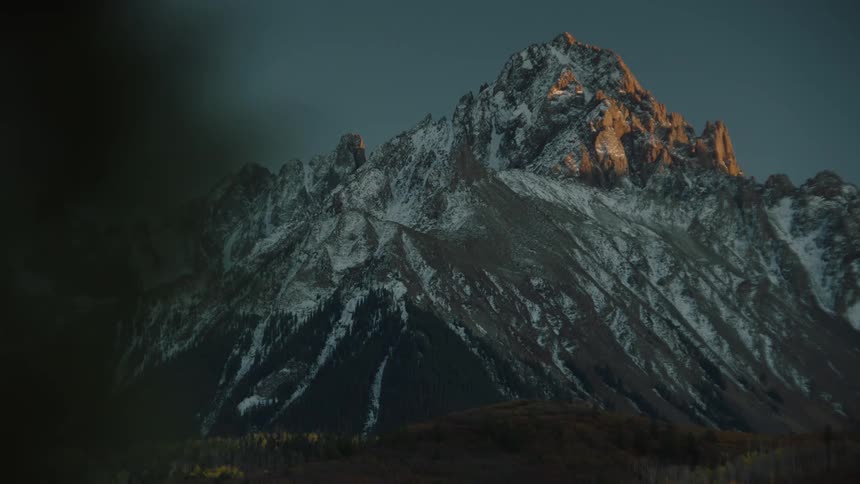 A rugged mountain peak with snow and the last light of sunset hitting its peak