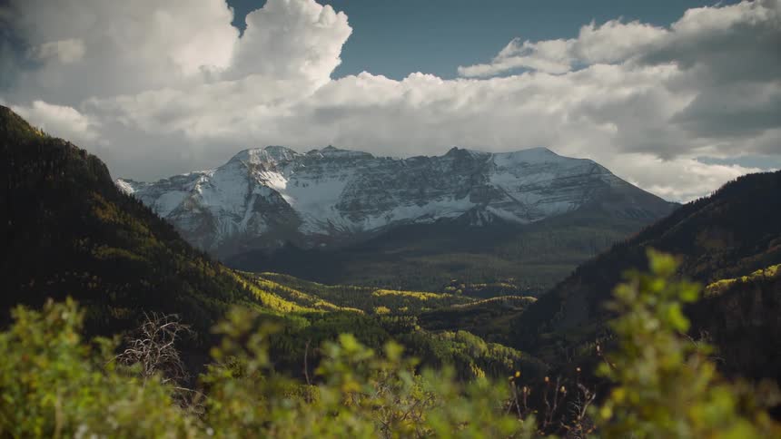 Wooded hills and in the background snowy mountain cliffs against a blue sky and clouds