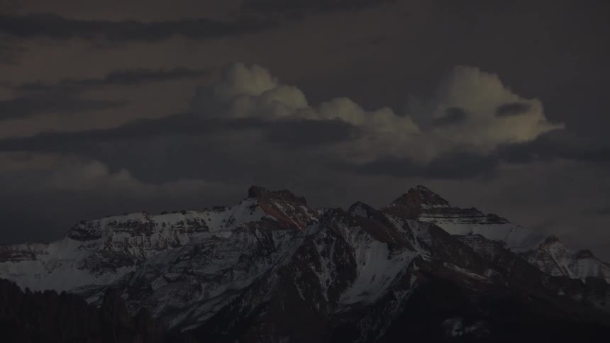 Clouds move over a snow covered mountain range as darkness falls