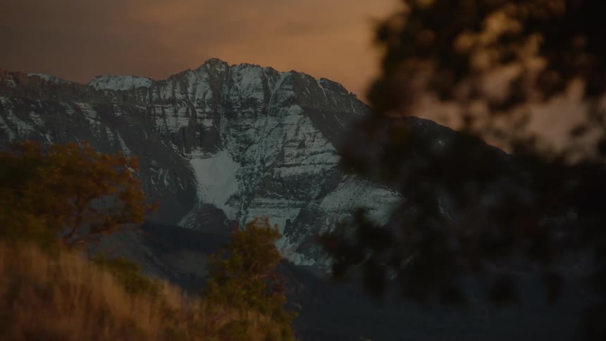 A panoramic view of a mountain range with peaks partially covered in snow at sunset