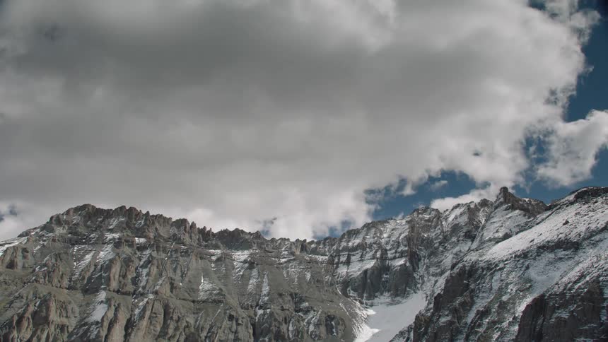 Time lapse of a snowcapped mountain peak under a blue sky with clouds