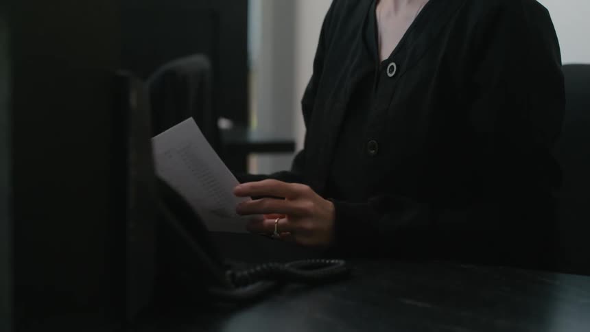 Woman sitting at an office desk holding a sheet of paper and making a phone call