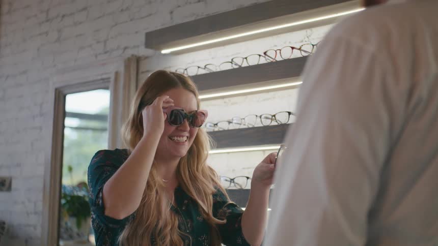 A woman with long hair tries sunglasses at a shop